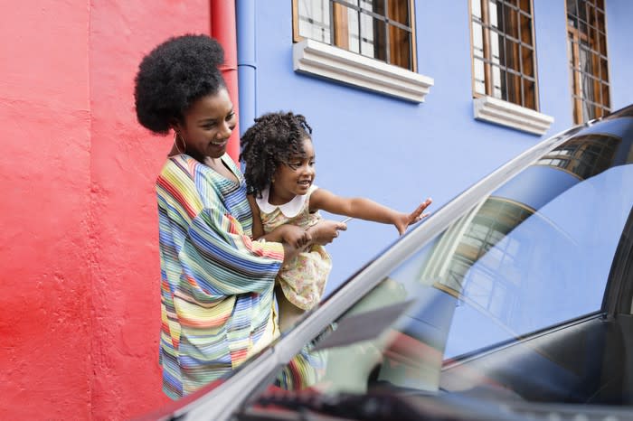 A woman with a little girl reaching toward a car.