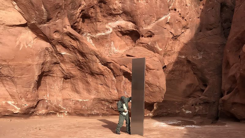 In this Nov. 18, 2020, file photo provided by the Utah Department of Public Safety, a Utah state worker stands next to a metal monolith in the ground in a remote area of red rock in Utah. The mysterious silver monolith that was placed in the Utah desert disappeared less than 10 days after it was spotted by wildlife biologists performing a helicopter survey of bighorn sheep, federal officials and witnesses said. The Bureau of Land Management said it had received credible reports that the three-sided stainless steel structure was removed on Nov. 27.