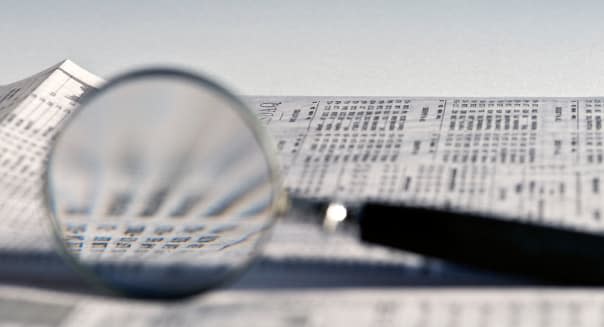 Magnifying glass highlighting stock quotes in business section of newspaper. Magnifying; glass; stock; business; section;