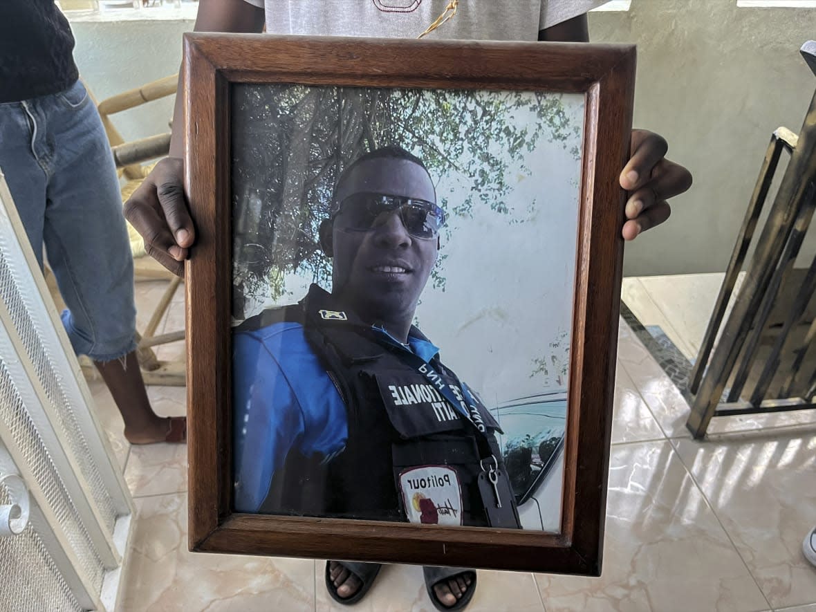 A photo of missing Haitian police Officer Ricken Staniclasse is held by his 11-year-old son at their home in Port-au-Prince, Haiti, Saturday, Jan. 21, 2023. One of Haiti’s gangs stormed a key part of the capital, Port-Au-Prince, and battled with police throughout the day, leaving at least three officers dead and another missing. (AP Photo/Megan Janetsky)