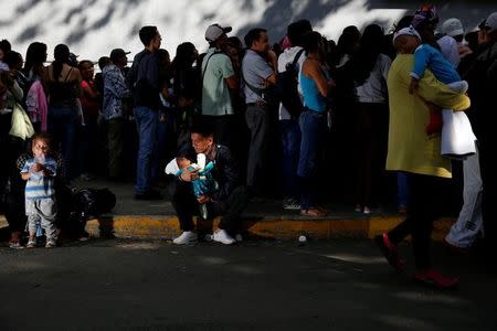Un hombre con un bebé en brazos descansa en la acera tras hacer fila para comprar pañales en Caracas. 18 de marzo de 2017. REUTERS/Carlos Garcia Rawlins