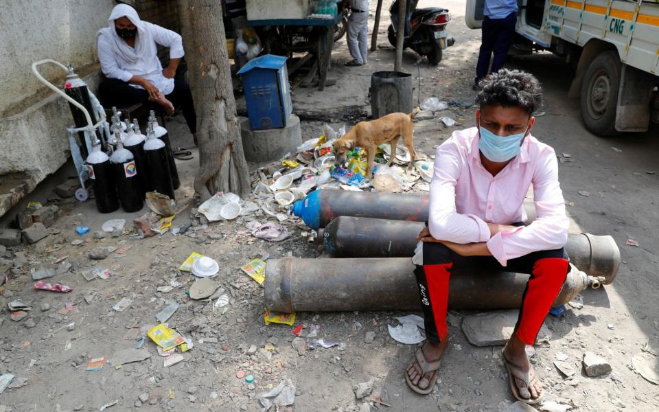 Sumit Kumar, 28, sits on an oxygen cylinder as he waits outside a factory in New Dehli to get it refilled - Reuters