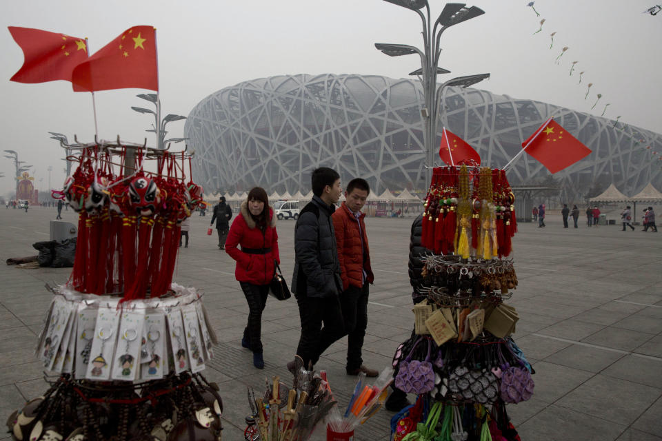 In this picture taken, Sunday, Feb. 23, 2014, tourists pass by memorabilia on sale near the iconic Bird's Nest National Stadium in Beijing, China. The National Stadium, nicknamed the Bird’s Nest because of its lattice design, has become a key Beijing landmark and a favored backdrop for visitors' snapshots. But few tourists are willing to pay more than $8 to tour the facility as enthusiasm for the 2008 Games fades, and the venue has struggled to fill its space with events. Beijing, which spent more than $2 billion to build 31 venues for the 2008 Summer Games, is reaping some income and tourism benefits from two flagship venues, though many sites need government subsidies to meet hefty operation and maintenance costs. (AP Photo/Ng Han Guan)
