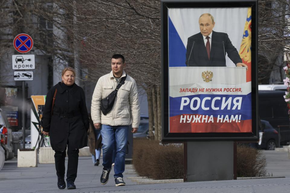 People walk past a billboard with an image of Russian President Vladimir Putin and words reading "The West doesn't need Russia, we need Russia!" in a street in Sevastopol, Crimea, Wednesday, March 6, 2024. The economy's resilience in the face of bruising Western sanctions is a major factor behind President Vladimir Putin's grip on power in Russia. (AP Photo)
