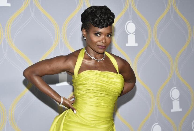 LaChanze in a bright yellow halter dress posing against a gray background with her hands on her hips