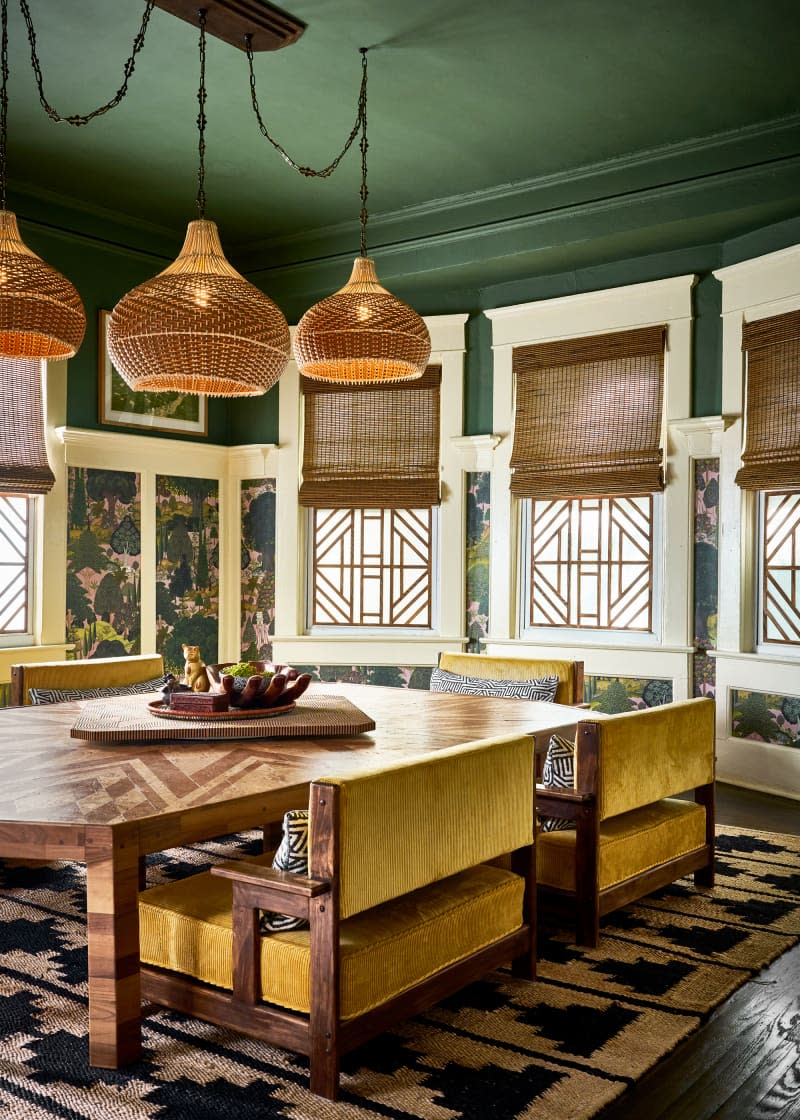 Green painted ceiling in dining room with mustard colored upholstered dining chairs.