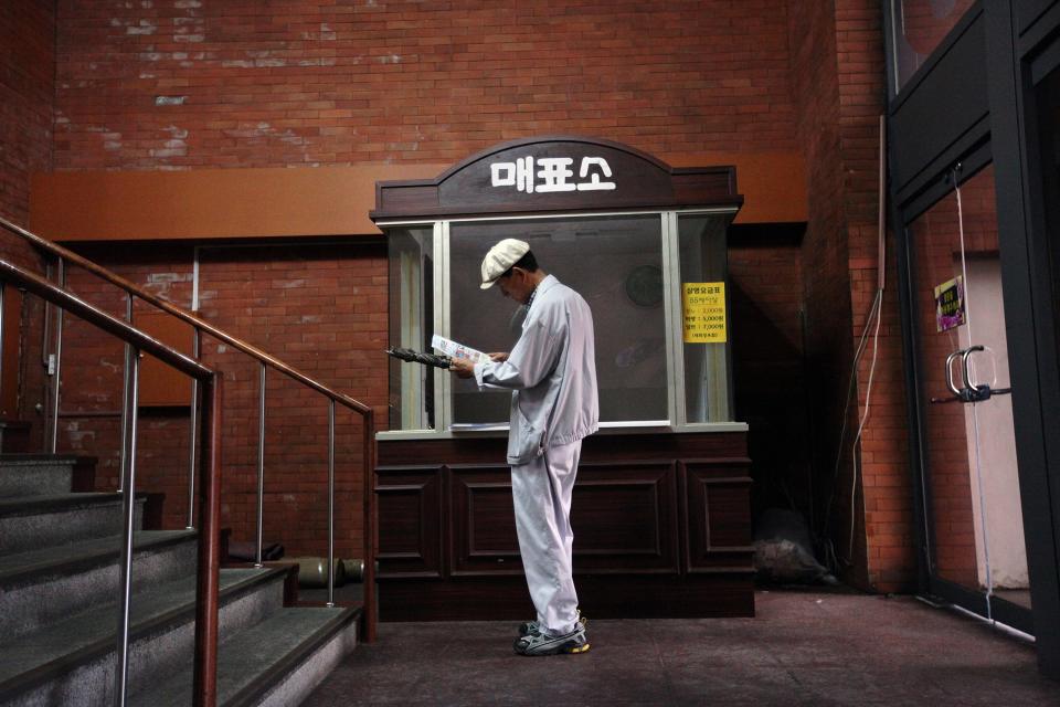 A patron reads a leaflet in front of a run-down ticket box at Seoul's last old-style one-screen cinema at Seodaemun Art Hall in Seoul, South Korea, Wednesday, July 11, 2012. Seoul's last old-style one-screen cinema, soon to be knocked down and replaced by a new tourist hotel, played its final movie Wednesday - the Italian classic "The Bicycle Thief."(AP Photo/Hye Soo Nah)