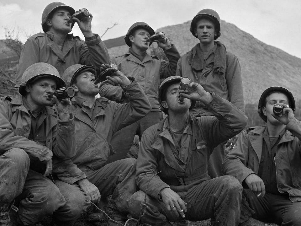 A group of US soldiers wearing helmets and fatigues drinking Coca Cola in Italy
