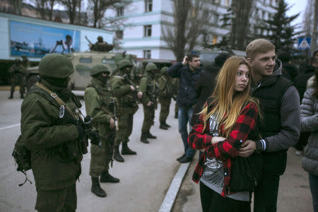 A couple stands next to armed servicemen outside a Ukrainian border guard post in Balaclava March 1, 2014. REUTERS/Baz Ratner