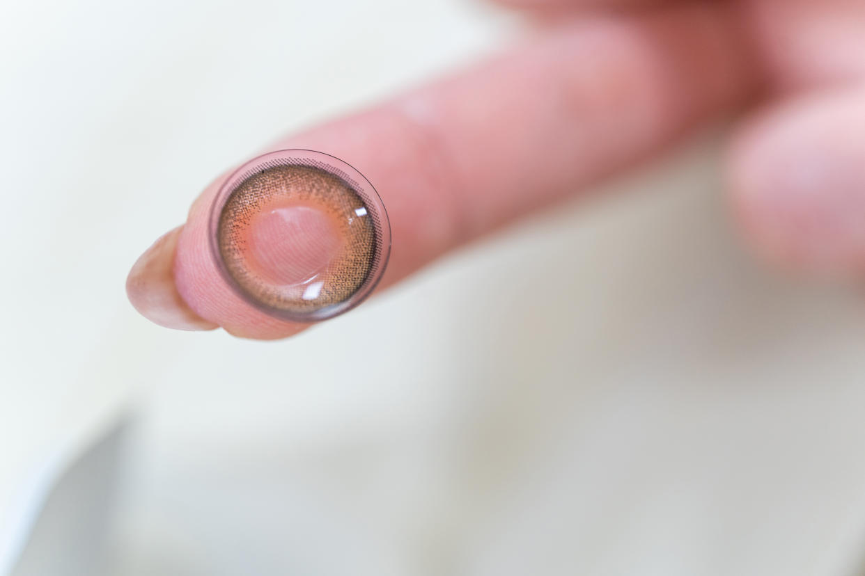 Japanese woman holds a brown contact lens for Halloween on her finger.