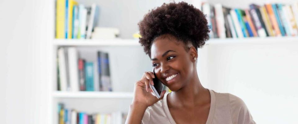 Laughing afro american young adult woman at mobile phone indoors at home