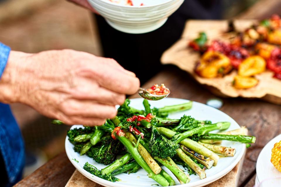 Someone spooning dressing over roasted broccoli.