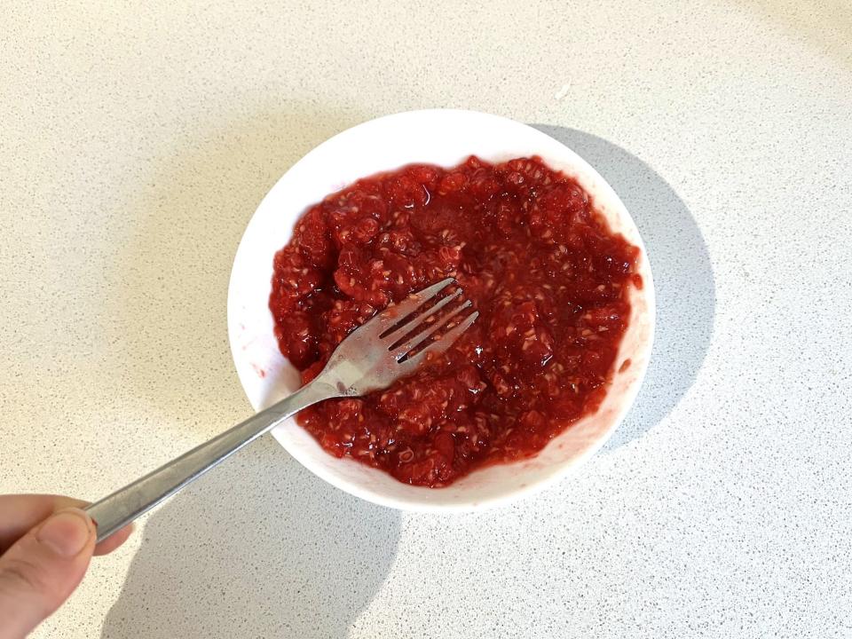 Raspberries being crushed with a spoon.