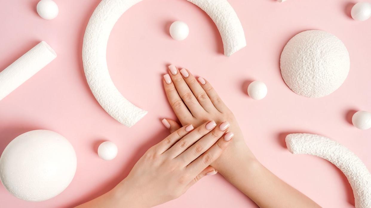 pink manicure and white abstract shapes on pink background, top view