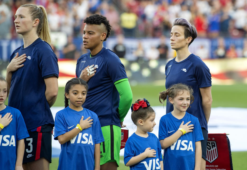 United States midfielder Samantha Mewis (3), goalkeeper Adrianna Franch, center, and forward Megan Rapinoe, right, stand with their jerseys turned inside out during the playing of the national anthem before a SheBelieves Cup women's soccer match against Japan, Wednesday, March 11, 2020 at Toyota Stadium in Frisco, Texas. (AP Photo/Jeffrey McWhorter)