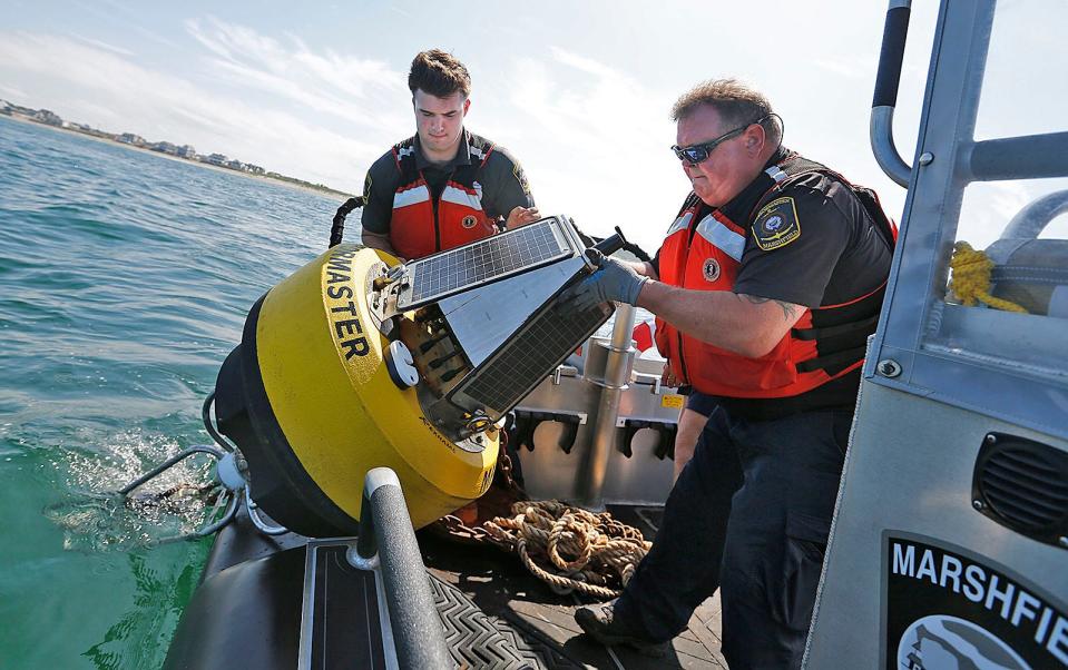 Jack Thompson and Rick Rodwell launch a shark-detecting buoy from a Marshfield harbormaster boat off Rexhame Beach.