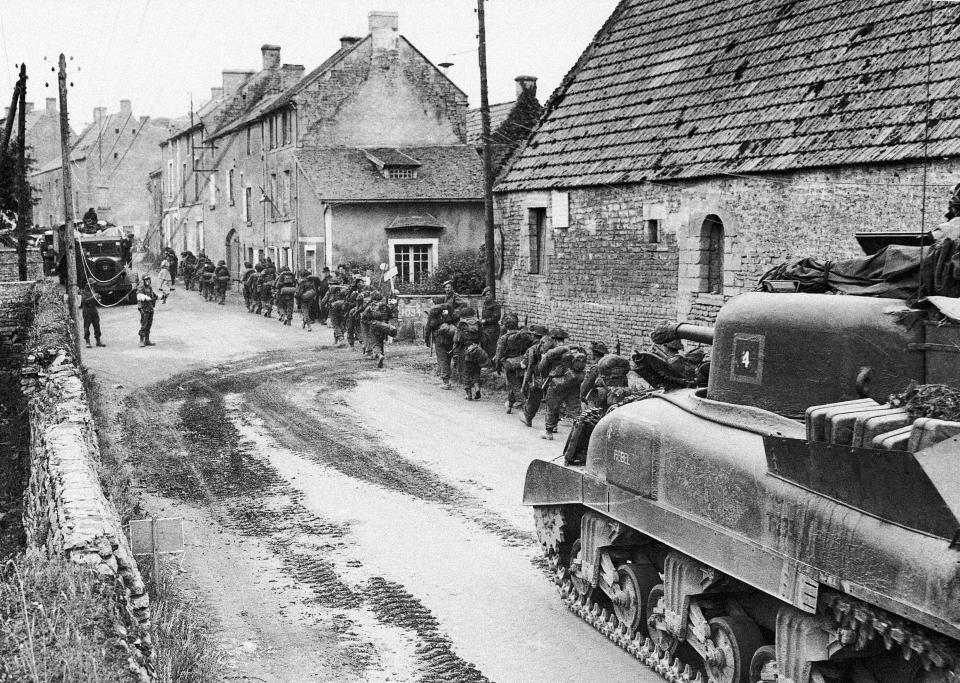 FILE - British troops and vehicles passing inland through a village in Normandy linemen are busy laying down communication cables while British, Canadian and U.S. Armour passes them en route for the frontline, on June 13, 1944. (AP Photo, File)