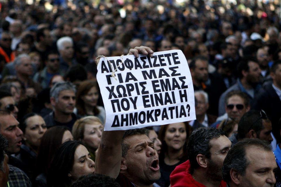 A protestor holds a banner that reads in Greek "You decide for us without us, where’s the democracy in that?" outside of Parliament during a strike to protest government plans to privatize the state-run organizations in capital Nicosia, Cyprus, Thursday, Feb. 27, 2014. Hundreds of protesters have gathered outside Cyprus' parliament to voice opposition against legislation that will pave the way for the privatization of state-owned companies. (AP Photo/Petros Karadjias)