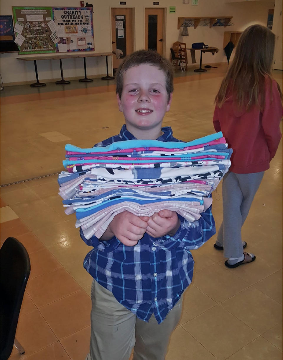 This Jan. 12, 2020 photo provided by Meg Hydock shows Gibson Griffith, 10, holding a stack of fabric crate liners he and others sewed to send to wildlife injured in wildfires in Australia in Lee, N.H. Griffith, who organized a sewing party is among thousands of people worldwide who have been making everything from bat wraps to kangaroo joey pouches for the animals affected by the wildfires. (Meg Hydock via AP)