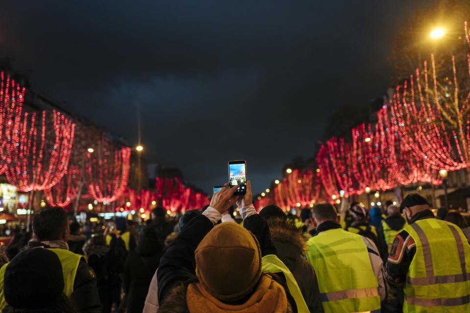 A demonstrator wears a yellow vest as she takes a photo on the Champs Elysees avenue in Paris, Saturday, Dec. 22, 2018. France's yellow vest protesters, who have brought chaos to Paris over the past few weeks with their economic demands, demonstrated in sharply reduced numbers Saturday at the start of the Christmas and New Year holidays. (AP Photo/Kamil Zihnioglu)