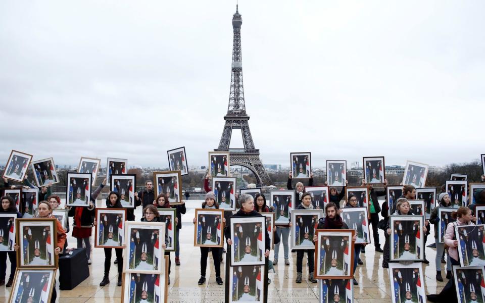  French climate activists hold inverted portraits of French President Emmanuel Macron during a Climate Change protest in front of the Eiffel Tower, calling for greater action among COP25 leaders to address climate change, in Paris - REUTERS/Benoit Tessier