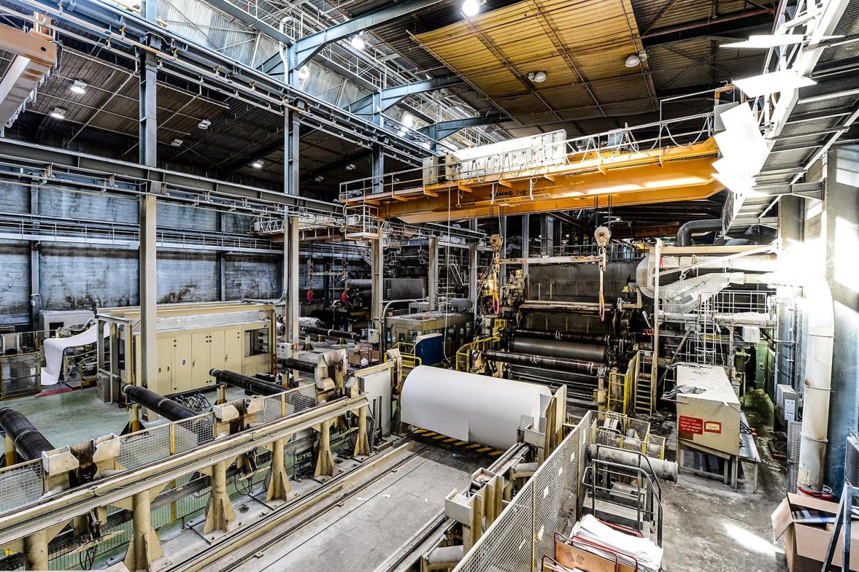 A paper factory with large machines and rollers is empty and quiet. 