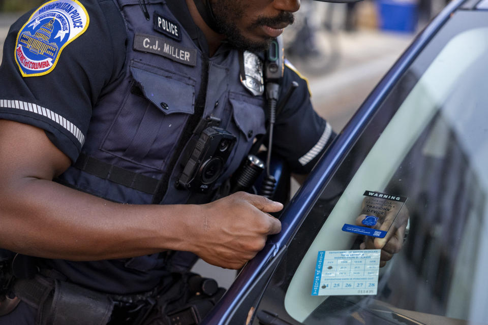 Metropolitan Police Department officer Cyrus Miller puts a sticker on a windshield during an event where police officers distributed Apple AirTags and similar tracking devices to drivers in an attempt to curb a rise in crime in Washington on Tuesday, Nov. 7, 2023. (AP Photo/Amanda Andrade-Rhoades)