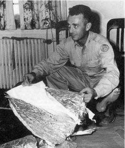 July 1947: Maj. Jesse A. Marcel of Houma, Louisiana, an officer of the 509th Bombardment Group at Roswell, New Mexico, inspects what was identified by a Fort Worth, Texas, Army Air Base weather forecaster as a ray wind target used to determine the direction and velocity of winds at high altitudes. Initial stories originating from Roswell, where the object was found, had labeled it a "flying disc" but inspection at Fort Worth revealed its true nature.