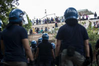 Police observe as migrants and Italians stand on the roof of an abandoned school before being evicted, on the outskirts of Rome, Monday, July 15, 2019. Residents set fire early Monday to mattresses and other garbage to form a barrier and prevent riot police from entering the building but authorities doused the blaze and proceeded with the eviction. (Massimo Percossi/ANSA via AP)