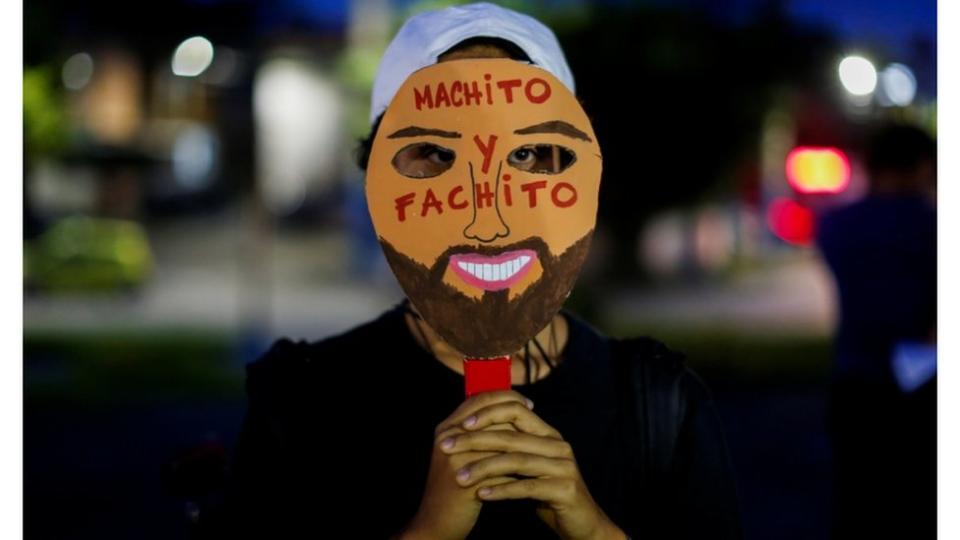 En una protesta contra medidas adoptadas por el gobierno de El Salvador, un joven hace alusión al presidente, Nayib Bukele, con una máscara que dice "machito y fachito".