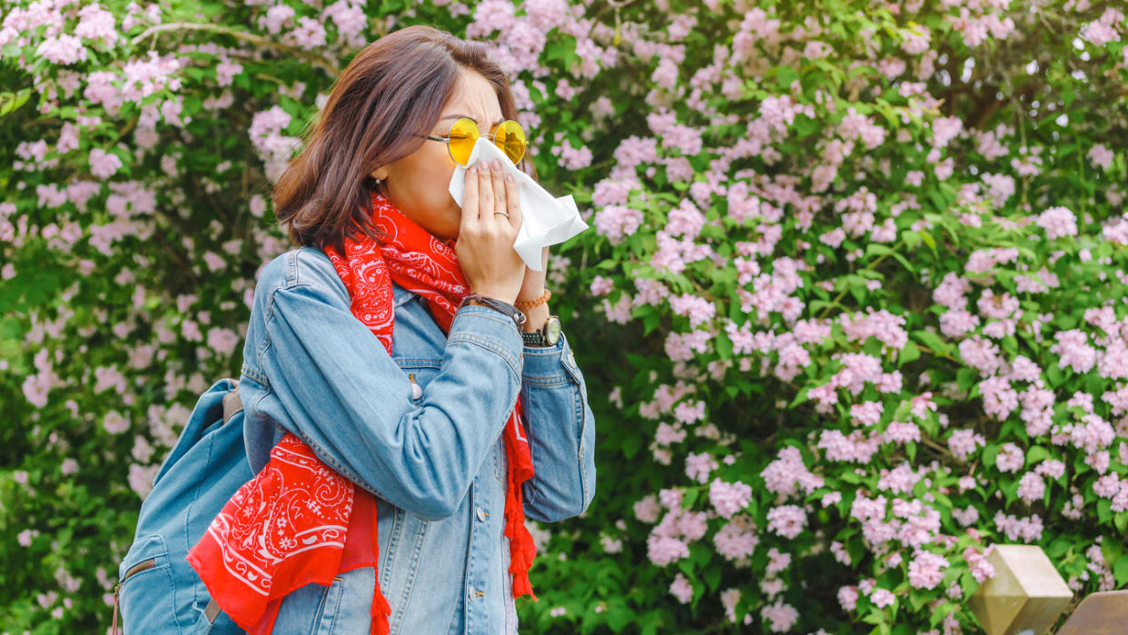 A person uses a handkerchief while standing near a blossoming tree.