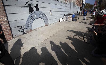 People take photos of a new art piece by British graffiti artist Banksy in the Brooklyn borough of New York, October 17, 2013. REUTERS/Carlo Allegri