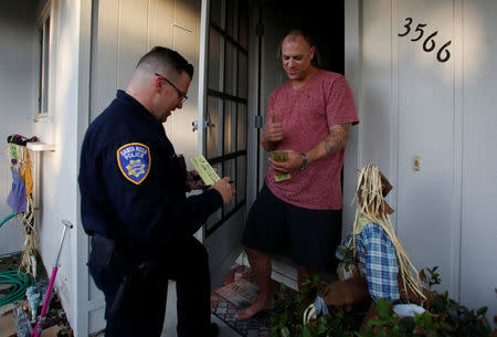 Patrick Seawright (R) reacts as he receives a pass from Santa Rosa police officer Travis Dunn that allows him to come and go from the evacuation zone he lives in after a wildfire tore through adjacent streets in Santa Rosa, California, U.S. October 15, 2017. REUTERS/Jim Urquhart