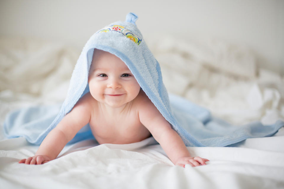 A smiling baby under a blue hooded towel.