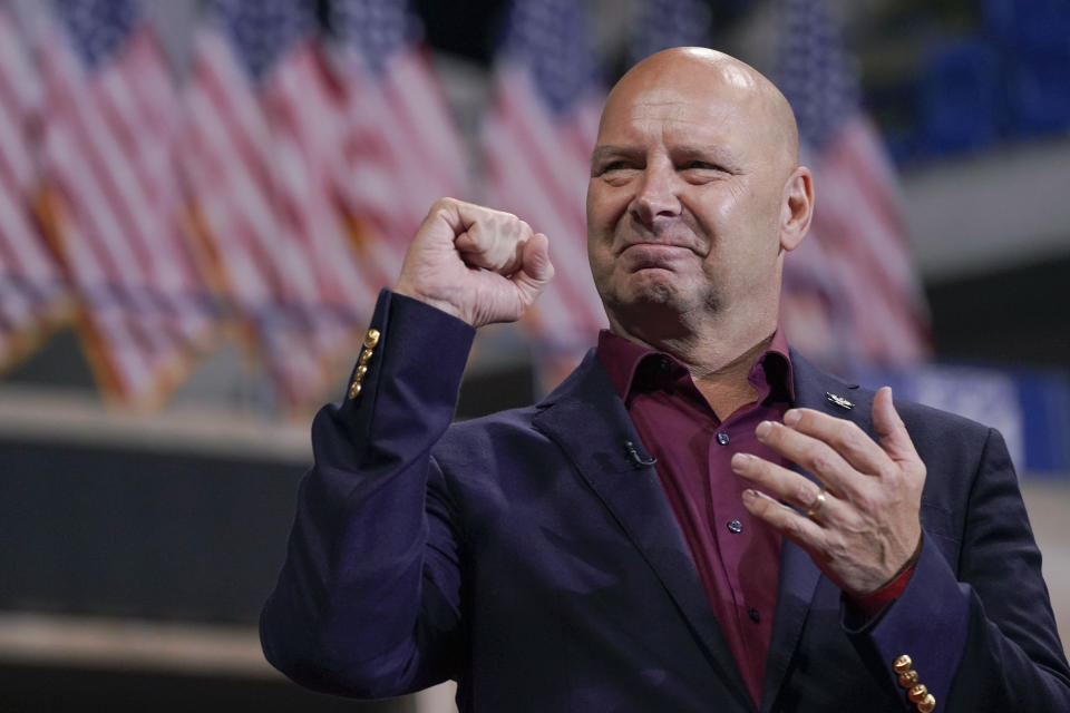 Doug Mastriano stands in front of a row of American flags at a rally.