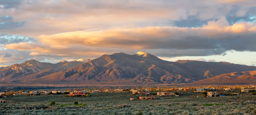 Panoramic view of distant mountains under a partly cloudy sky with scattered houses and vegetation in the foreground