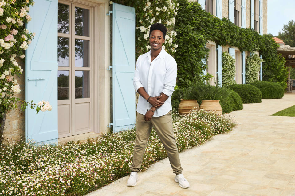 Marcellus posing in front of a Greek house with blue shutters.