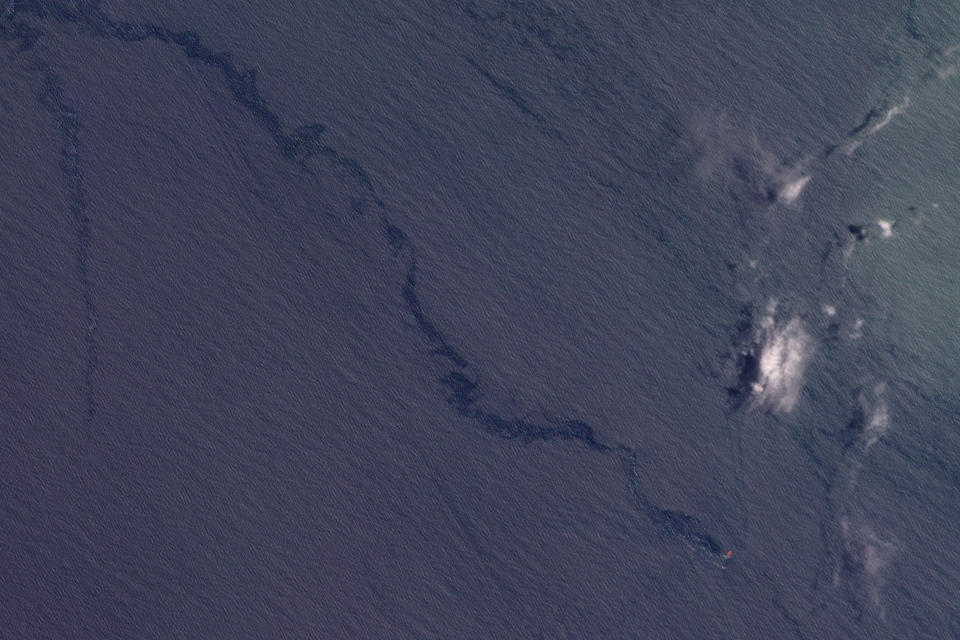 This satellite image from Planet Labs shows an oil spill drifting from the wreckage of the Trinity Spirit ship, lower right to upper left, with clouds at right, on April 16, 2022, following an explosion aboard the ship in February 2022. The ship was used to store and refine large quantities of oil extracted from the ocean floor and moored 15 miles off the coast of Nigeria. The vessel was carrying 40,000 barrels of oil. (Planet Labs via AP)