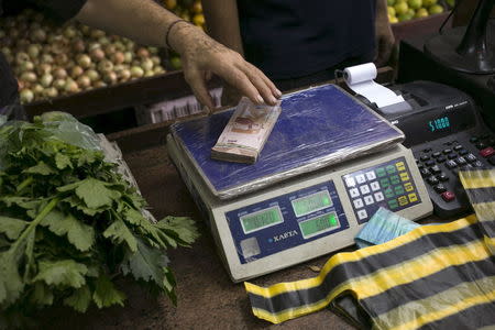 A clerk grabs a stack of Venezuelan 10 bolivars banknotes at a fruit and vegetable store in Caracas July 10, 2015. REUTERS/Marco Bello