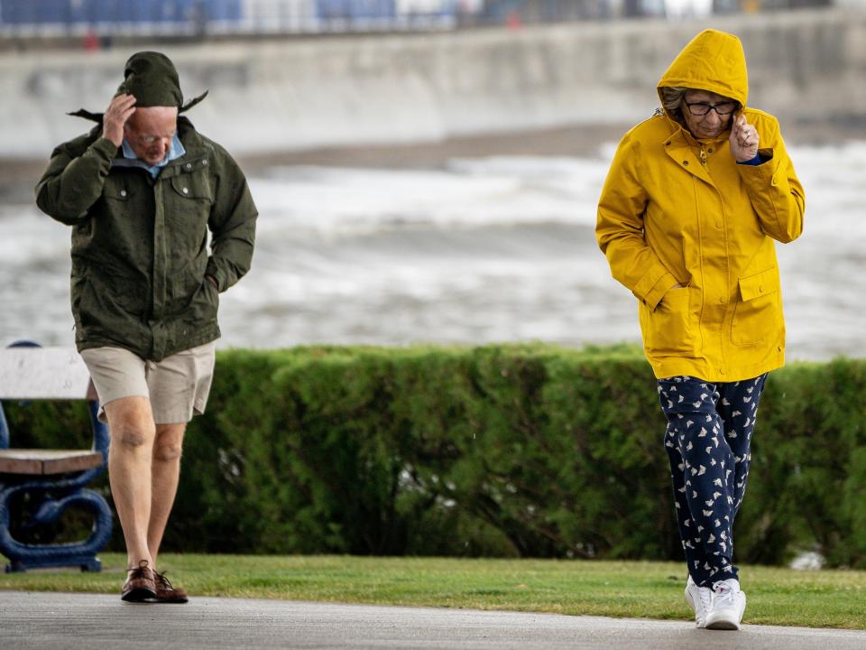 People pull down their hoods to shelter from the wind as they walk along the sea front in Porthcawl, Wales (PA)