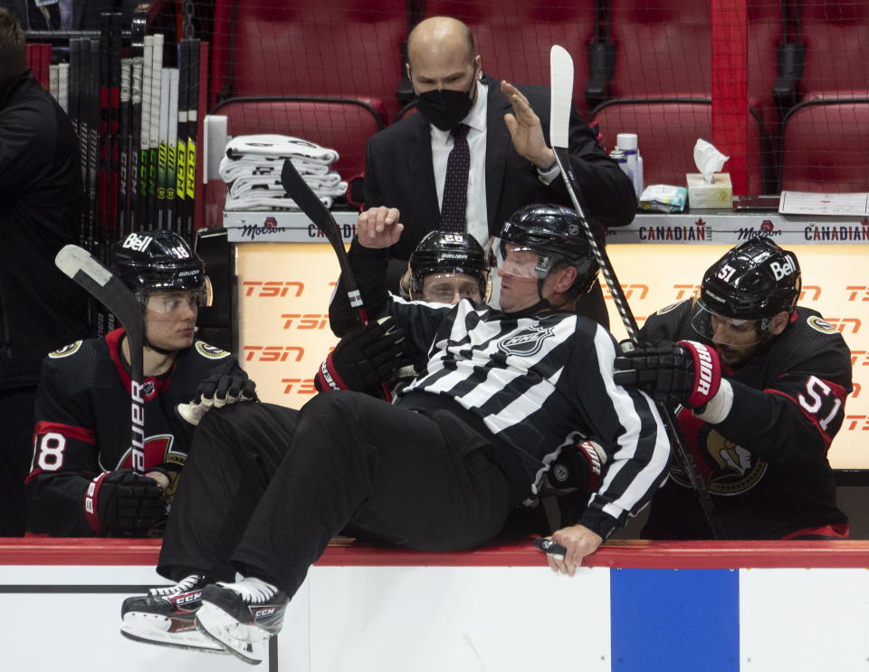 Ottawa Senators players help linesman Derek Nansen as he falls into the bench while avoiding a shot along the boards during the second period of an NHL hockey game between the Senators and the Edmonton Oilers on Wednesday, April 7, 2021, in Ottawa, Ontario. (Adrian Wyld/The Canadian Press via AP)
