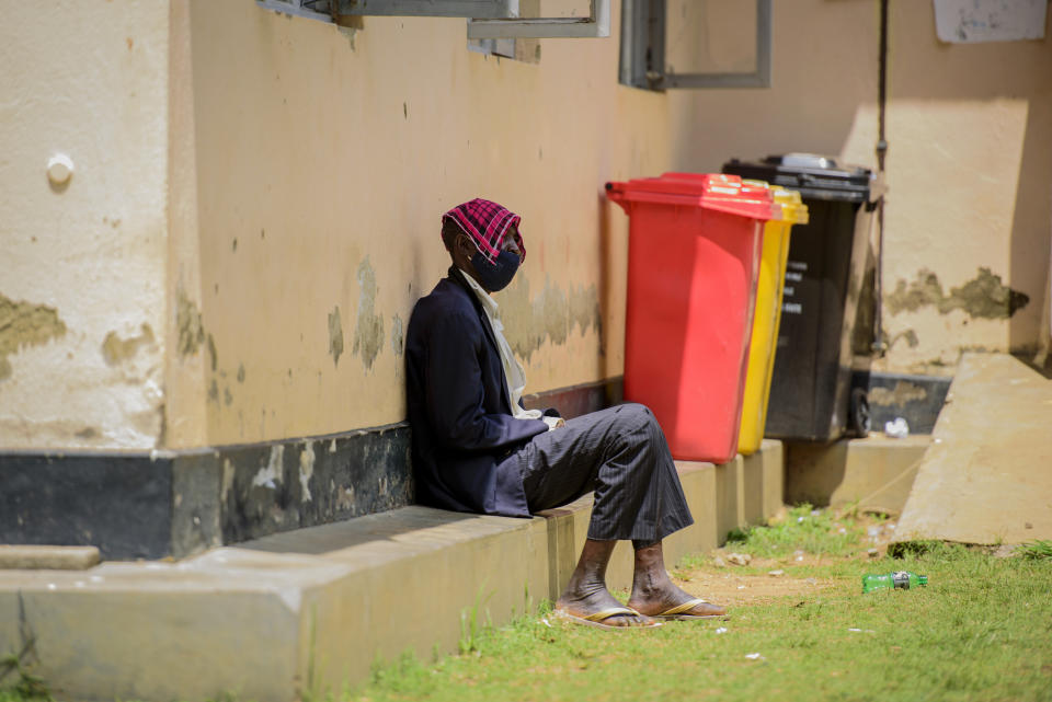 A man waits in a small patch of shade to be vaccinated against the coronavirus at Awach Health Center in Gulu, Uganda Wednesday, Sept. 22, 2021. Because a vial contains seven doses that must be accounted for, vaccines are not distributed until seven people are in line. So people come and go without a getting a jab. (AP Photo/Nicholas Bamulanzeki)