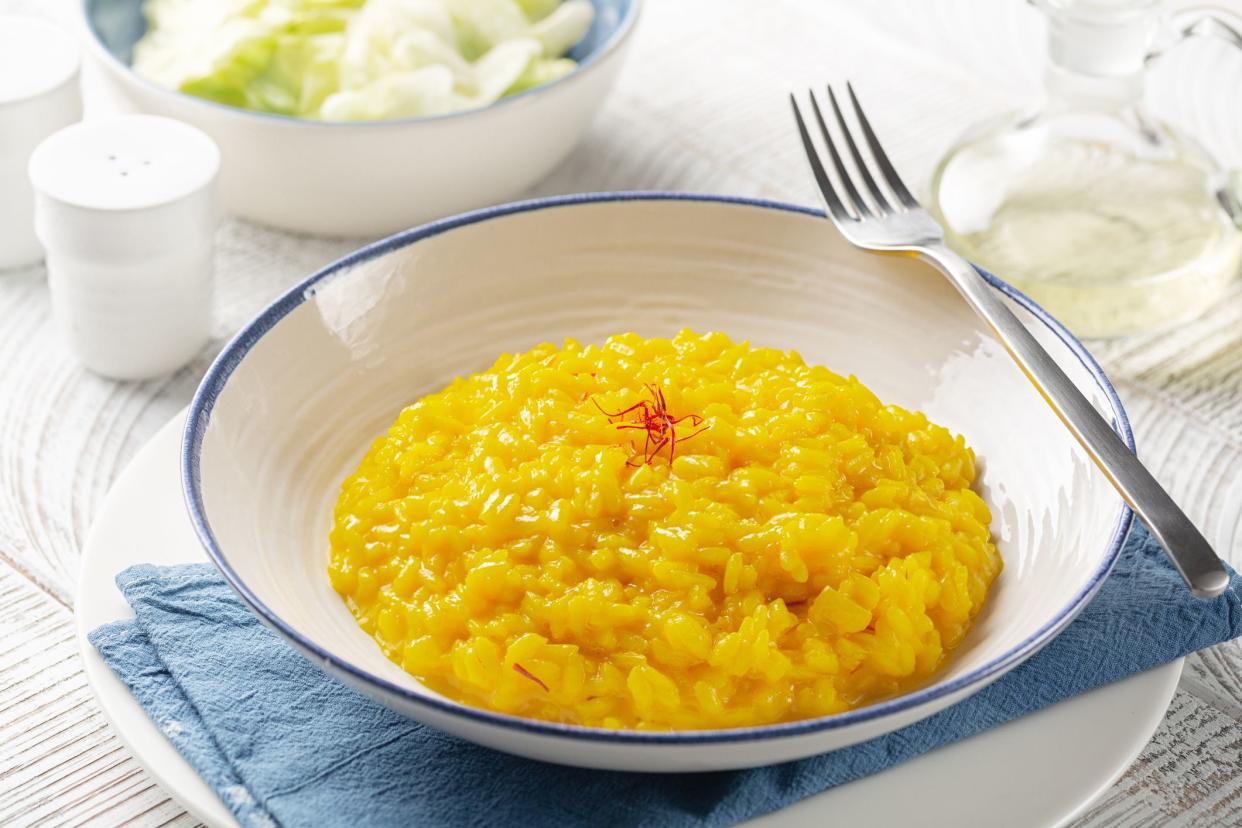 Dinner with risotto alla milanese and fresh salad. Italian dish made from saffron, rice, butter, hard cheese and vegetable broth. White table.