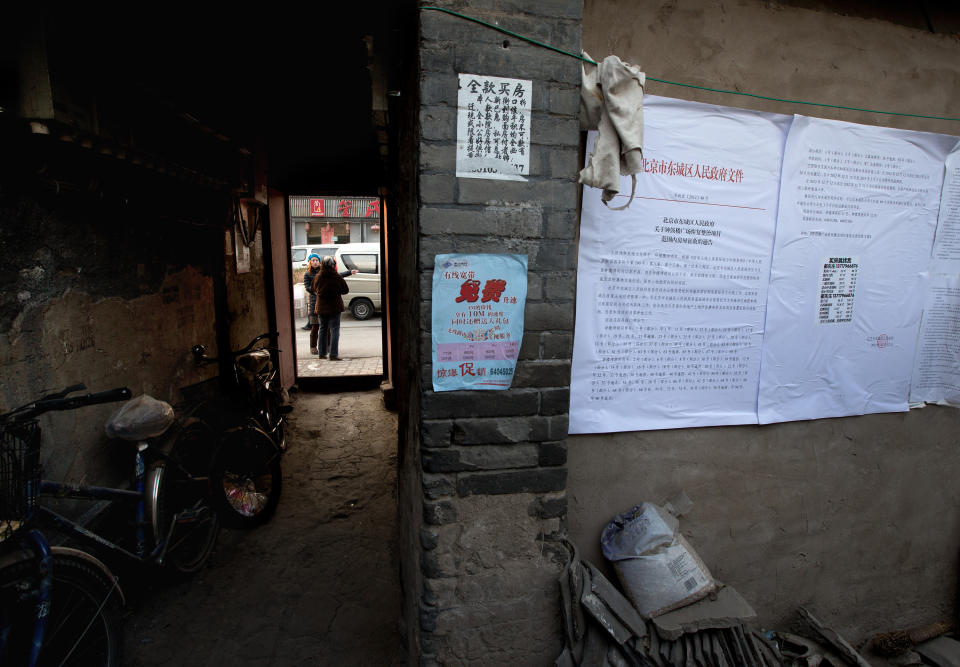 In this photo taken on Dec. 26, 2012, people chat outside a Hutong home as a demolition notice is placed on the wall near the historical Drum and Bell Tower in Beijing. The district government wants to demolish these dwellings, move their occupants to bigger apartments farther from the city center and redevelop a square in 18th century Qing Dynasty fashion. (AP Photo/Andy Wong)