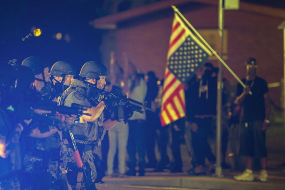 <p>A police officer raises his weapon at a car speeding in his general direction as a more vocal and confrontational group of demonstrators stands on the sidewalk during further protests in reaction to the shooting of Michael Brown near Ferguson, Missouri August 18, 2014. (Lucas Jackson/Reuters) </p>