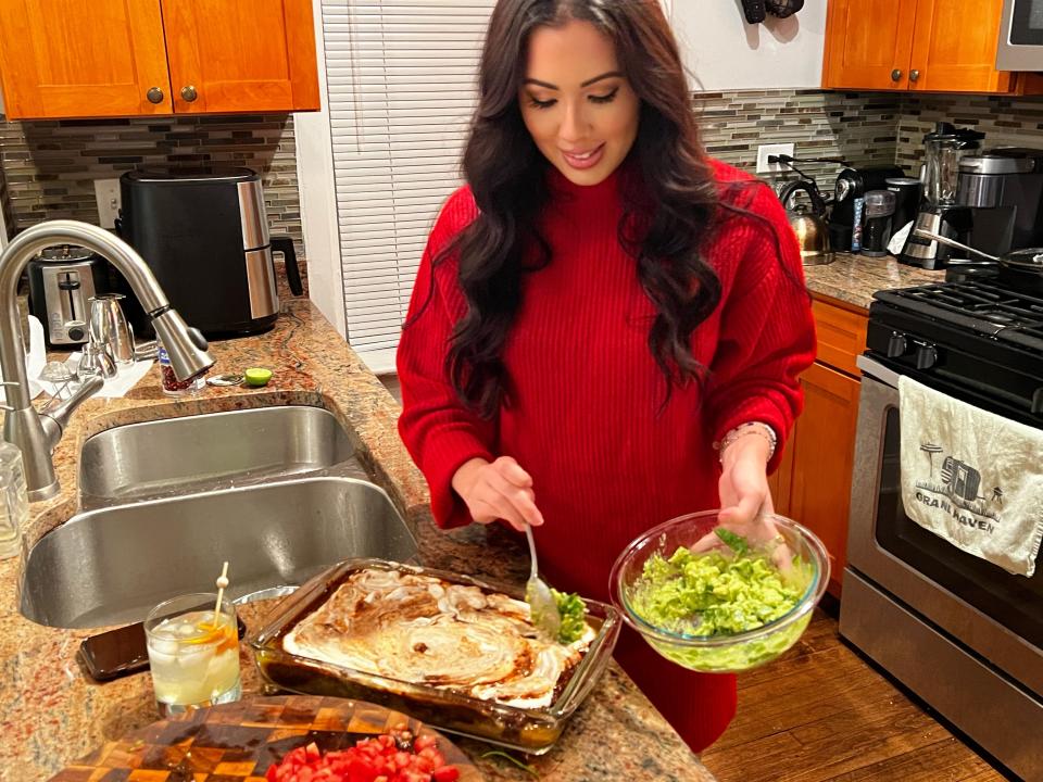 The writer spoons a guacamole mix on top a casserole dish filled with a dip containing beans and sour cream