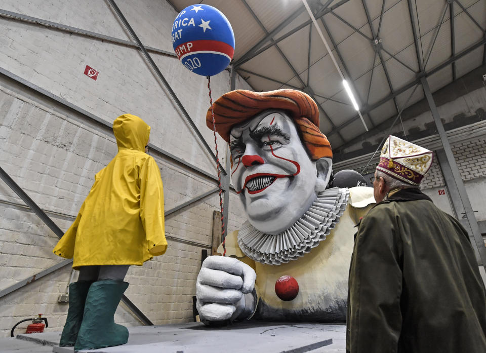 A satiric carnival float depicting US President Donald Trump as horror clown Pennywise is watched by a reveller during a preview in a hall in Cologne, Germany, Tuesday, Feb. 18, 2020. The traditional carnival parades on Rosemonday make fun of politics and are watched by hundreds of thousands in the streets of Cologne, Duesseldorf and Mainz. (AP Photo/Martin Meissner)