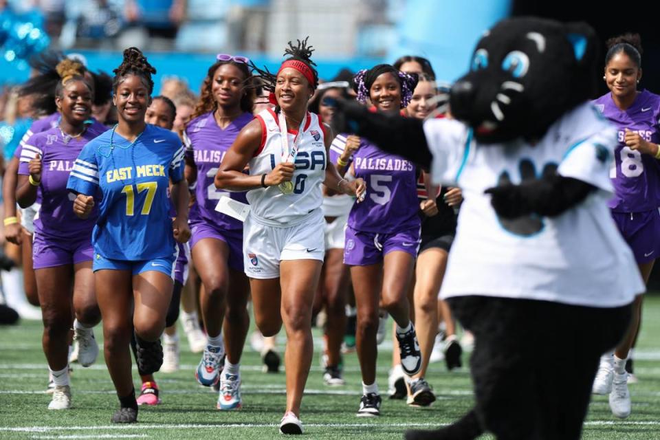 Amber Clark, center, a North Carolina native and gold-medal winning USA Football flag football athlete, leads a group of CMS flag football-playing girls out of the tunnel at a Carolina Panthers game in Bank of America Stadium in Charlotte in August 2023. Melissa Melvin-Rodriguez/mrodriguez@charlotteobserver.com