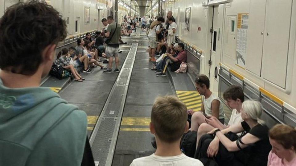 大批旅客「大包小包」在隧道內等待，甚至有人乾脆席地而坐。（圖／翻攝自BBC）
