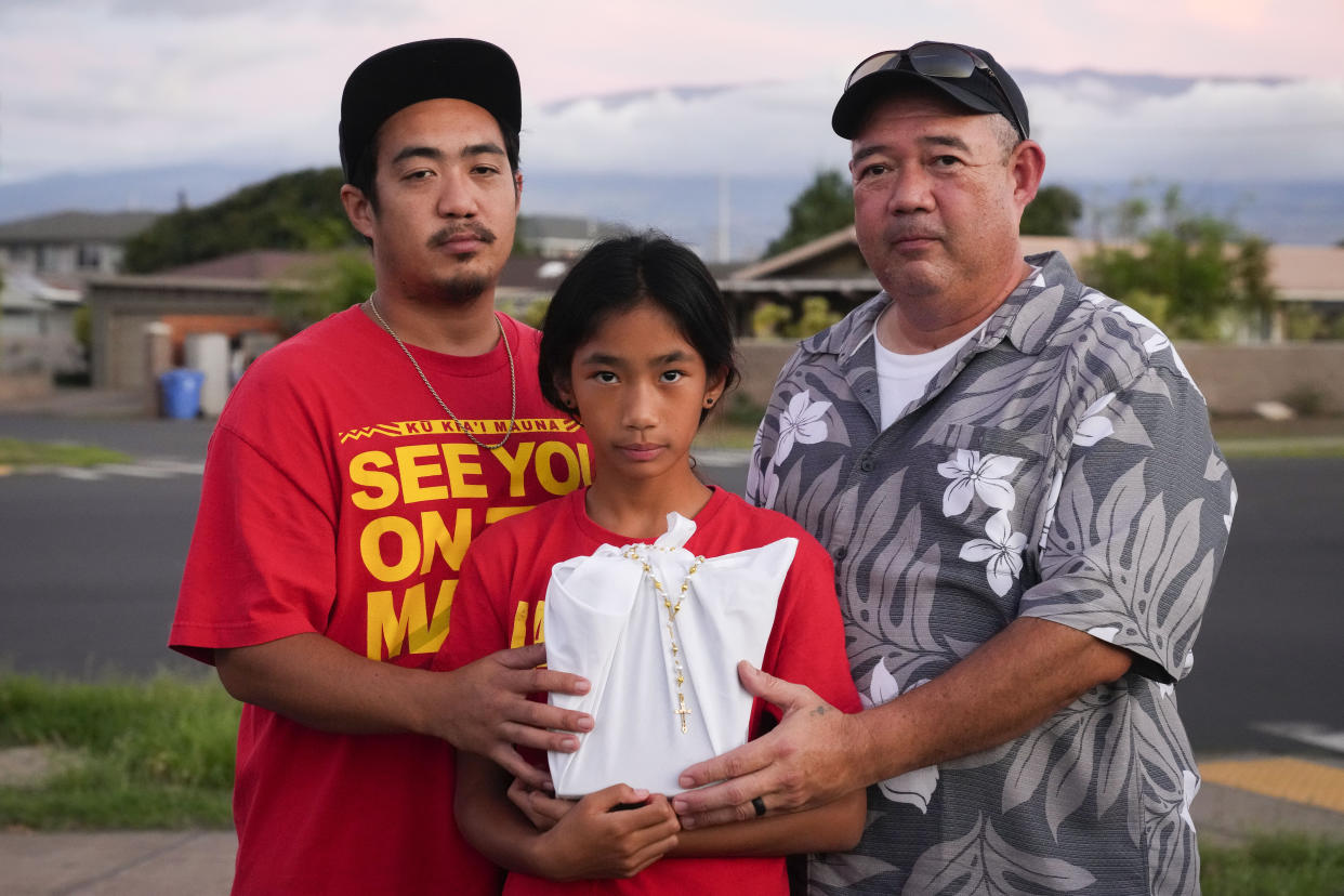 FILE - Briena Mae Rabang, 10, holds the ashes of her great-grandmother Sharlene Rabang, who was named as the 100th victim of the Lahaina wildfire, while posing for a photo with her father Branden, left, and grandfather Brandon, right, Friday, Dec. 8, 2023, in Kahului, Hawaii. (AP Photo/Lindsey Wasson, File)